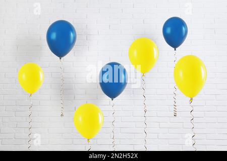 Viele Ballons in den Farben der ukrainischen Flagge in der Nähe der weißen Backsteinmauer Stockfoto