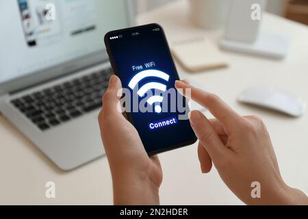 Frau, die sich mit einem Mobiltelefon am Tisch mit WLAN verbindet, Nahaufnahme Stockfoto