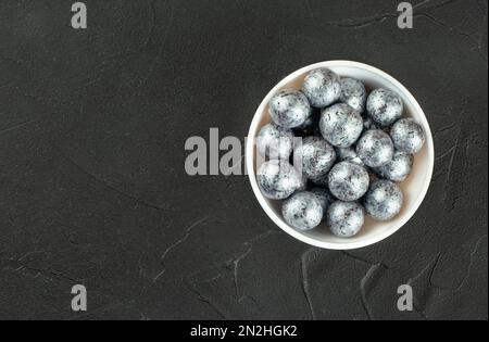 Silberne Süßigkeiten Haselnüsse in Schokolade in einer weißen Keramikschüssel auf Betonhintergrund, Kopierraum. Stockfoto