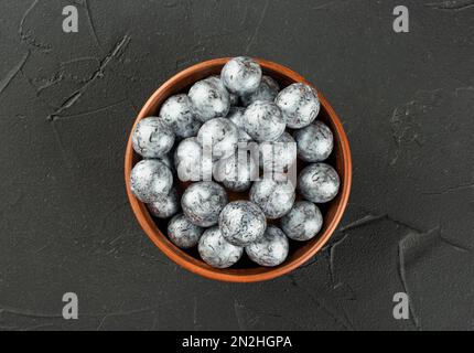 Große Schüssel mit silbernen Süßigkeiten Haselnüssen in Schokolade auf dunklem Betonhintergrund, Draufsicht. Stockfoto