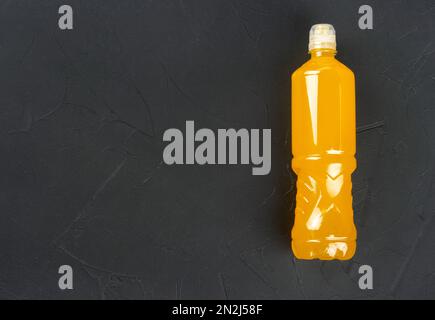 Plastikflasche mit orangefarbenem isotonischem Getränk für Sport auf dunklem Betonhintergrund. Speicherplatz kopieren. Stockfoto