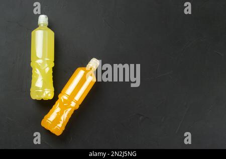 Zwei Plastikflaschen mit zitronenfarbenen und orangefarbenen isotonischen Getränken auf dunklem Betonhintergrund. Speicherplatz kopieren. Draufsicht Stockfoto