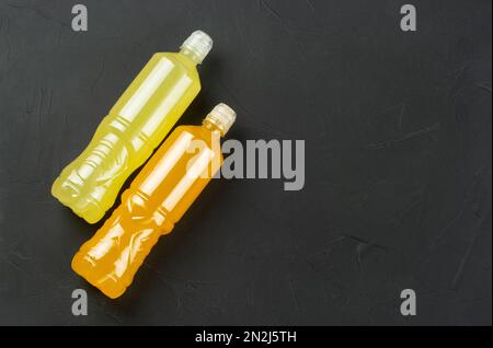Plastikflaschen mit Zitronen- und orangefarbenen isotonischen Getränken auf dunklem Betonhintergrund. Speicherplatz kopieren. Draufsicht Stockfoto