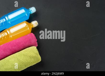 Blau-orangefarbenes isotonisches Getränk für Sport mit zwei Handtüchern auf dunklem Betonhintergrund, Kopierbereich. Stockfoto