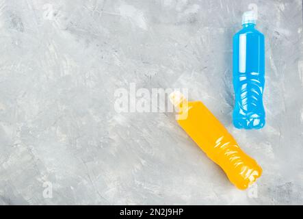 Zwei Plastikflaschen und blaue und orangefarbene isotonische Getränke auf hellem Hintergrund, Draufsicht, Kopierbereich. Stockfoto