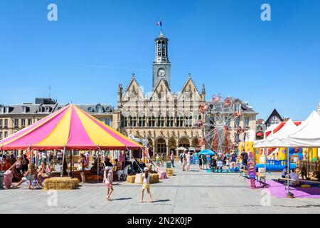 Fassade im gotischen Stil des Rathauses von Saint-Quentin, Frankreich, mit dem Circus Parc Sommerunterhaltung im Vordergrund an einem sonnigen Tag. Stockfoto