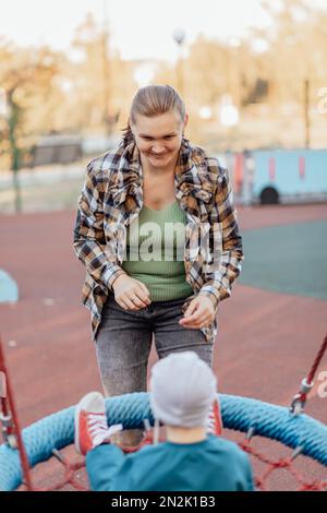 Ein kleiner Junge kletterte mit seiner Mutter auf die Treppe zur Rutsche Stockfoto