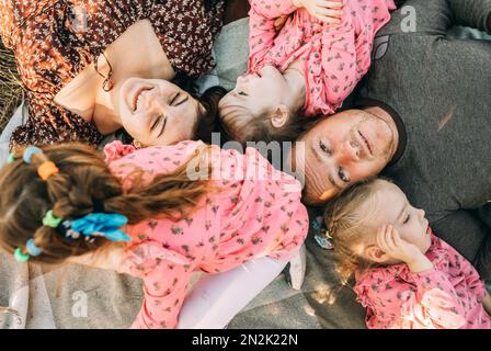 Eine glückliche Familie mit dreifarbigen Mädchen liegt im Park und entspannt sich im Freien Stockfoto