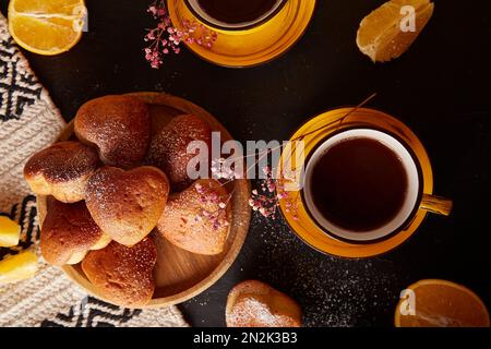 Teezeit mit gelben Tassen und hausgemachten herzförmigen Muffins. Cupcakes mit Orangengeschmack zum Valentinsfrühstück Stockfoto