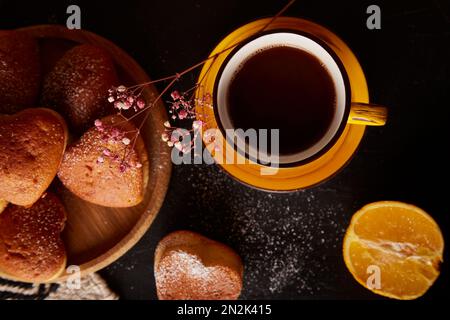 Gelbe Tasse mit Kaffee und hausgemachten herzförmigen Muffins. Cupcakes mit Orangengeschmack zum Valentinstag. Stockfoto