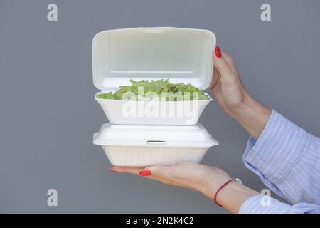 Frauenhände, die die Lunchbox mit Schaumstoff zum Mitnehmen offen halten, mit gesundem, frischem grünen Salat darin. Stockfoto