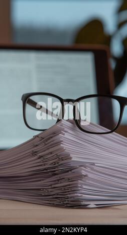 Zusammenstellung eines Stapels von Papieren, sortiert mit Büroklammern, Gläser in der Nähe des Laptops auf dem Schreibtisch. Arbeitsbereich, Geschäftstechnologie, Dokumente, Überarbeit Stockfoto