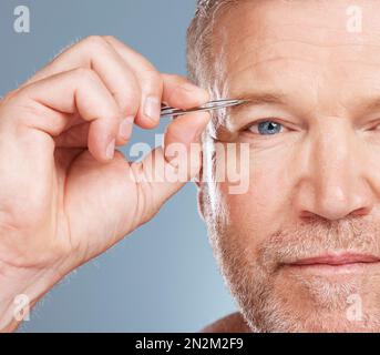 Gesicht, Porträt und Mann mit Augenbrauenpinzette im Studio isoliert auf blauem Hintergrund für Wellness. Gesundheit, Pflege und Senior männliches Modell mit Stockfoto