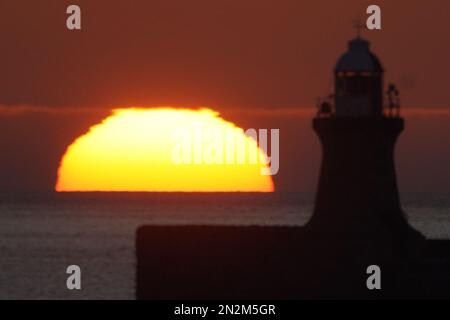 Die Sonne beginnt hinter dem Leuchtturm von South Shields an der Nordostküste Englands aufzugehen. Foto: Dienstag, 7. Februar 2023. Stockfoto