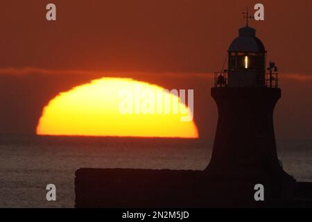 Die Sonne beginnt hinter dem Leuchtturm von South Shields an der Nordostküste Englands aufzugehen. Foto: Dienstag, 7. Februar 2023. Stockfoto