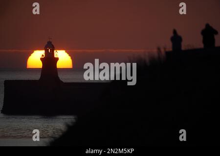 Die Menschen beobachten, wie die Sonne hinter dem Leuchtturm von South Shields an der Nordostküste Englands aufgeht. Foto: Dienstag, 7. Februar 2023. Stockfoto