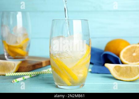 Füllen Sie Natronwasser in Glas mit Zitronenscheiben und Eiswürfeln auf einem hellblauen Holztisch Stockfoto