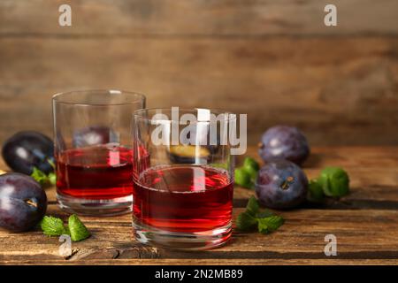 Köstlicher Pflaumenlikör, Minze und reife Früchte auf einem Holztisch. Hausgemachtes, starkes alkoholisches Getränk Stockfoto