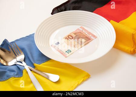 Die Flaggen der Ukraine und Deutschlands liegen in der Nähe eines Tellers mit 10 Euro auf weißem Hintergrund, Wirtschaft und Finanzen, finanzielle Unterstützung für die Ukraine Stockfoto