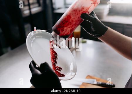 Salatzubereitung. Der Koch gießt Soße auf einen weißen Teller. Stockfoto