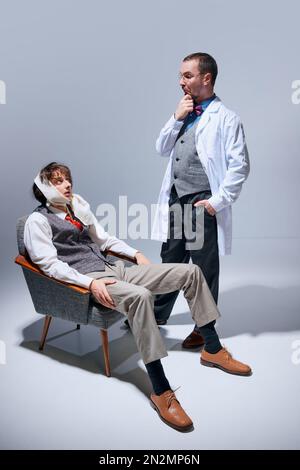 Befragungsgesicht. Junger Mann mit Zahnschmerzen beim Zahnarzt, Doktor. Medizinische Behandlung. Modelle vor grauem Studiohintergrund Stockfoto