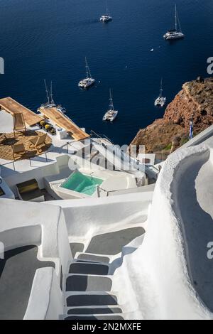 Stufen hinunter zu einer Hafenlandung mit Booten, die in der alten vulkanischen Caldera im Meer an der Küste des Dorfes Oia, Insel Santorini, Griechenland, festgemacht sind Stockfoto