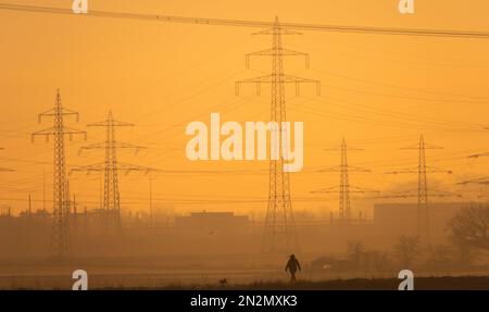 Hohenhameln, Deutschland. 07. Februar 2023. Bei Sonnenaufgang führt ein Streuner seinen Hund vor Hochspannungsleitungen in der Region Hannover. Kredit: Marco Rauch/dpa/Alamy Live News Stockfoto