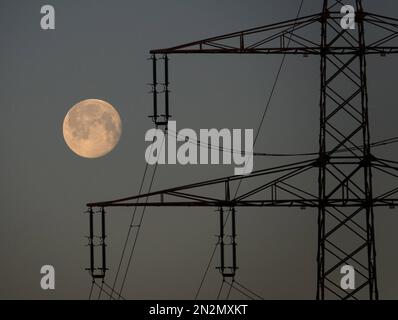 Hohenhameln, Deutschland. 07. Februar 2023. Der Mond ist am frühen Morgenhimmel hinter einer Hochspannungsleitung im Bezirk Peine. Kredit: Marco Rauch/dpa/Alamy Live News Stockfoto