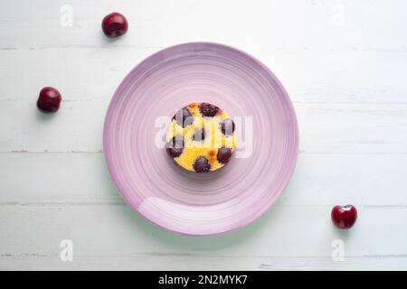 Cherry Clafoutis ist ein gebackenes französisches Obstdessert, traditionell schwarze Kirschen, auf einem Butterteller angeordnet und mit einem dicken Vanilleschoten bedeckt Stockfoto