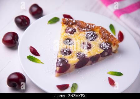 Cherry Clafoutis ist ein gebackenes französisches Obstdessert, traditionell schwarze Kirschen, auf einem Butterteller angeordnet und mit einem dicken Vanilleschoten bedeckt Stockfoto