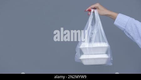 Frauenhände mit PVC-Plastiktüte und Lunchboxen aus Schaumstoff zum Mitnehmen. Einweg-Lebensmittelbehälter, Spendenkonzept. Stockfoto