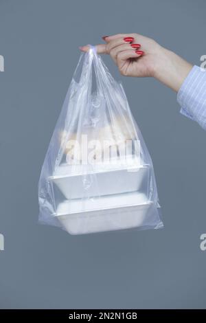 Frauenhände mit PVC-Plastiktüte und Lunchboxen aus Schaumstoff zum Mitnehmen. Einweg-Lebensmittelbehälter, Spendenkonzept. Stockfoto