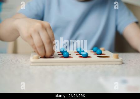Nahaufnahme der Hände eines unerkennbaren Kindes, das ein Spiel zur Entwicklung von Gedächtnis und Denken spielt. Ökologisches Spielzeug aus Holz Stockfoto