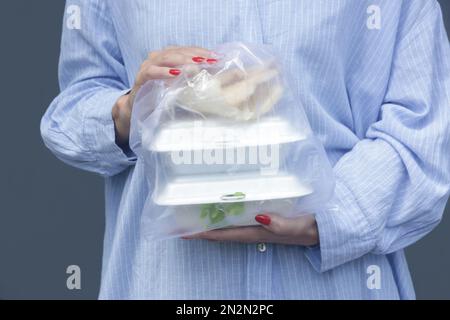 Frauenhände mit PVC-Plastiktüte und Lunchboxen aus Schaumstoff zum Mitnehmen. Einweg-Lebensmittelbehälter, Spendenkonzept. Stockfoto