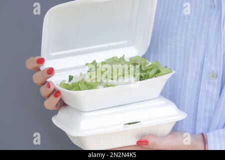 Frauenhände, die die Lunchbox mit Schaumstoff zum Mitnehmen offen halten, mit gesundem, frischem grünen Salat darin. Stockfoto