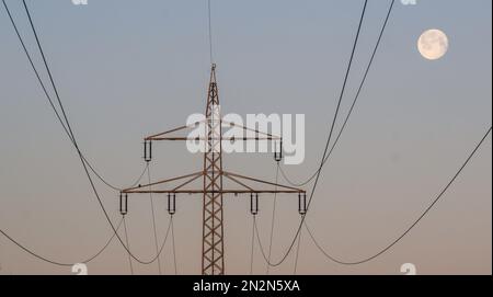 Hohenhameln, Deutschland. 07. Februar 2023. Der Mond ist am frühen Morgenhimmel hinter einer Hochspannungsleitung im Bezirk Peine. Kredit: Julian Stratenschulte/dpa/Alamy Live News Stockfoto