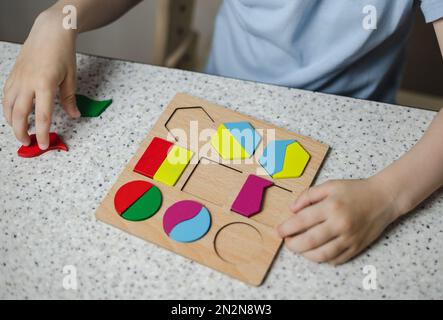 Nahaufnahme der Hände eines nicht erkennbaren Kindes, das Holzblöcke in die Rillen des Lernspielzeugs steckt. Das Konzept der Kindererziehung. Stockfoto