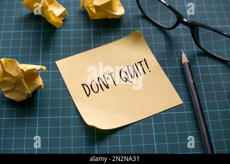 Papierkorb, Brille, Bleistift und eine gelbe Papiernotiz mit „Don't Quit“ auf einer grünen Handwerkermatte. Stockfoto