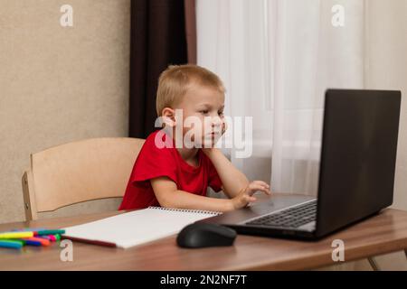 Online-Fernunterricht. Das Kind schaut sich den Laptop genau an und studiert die Zeichenstunde online im Internet. Online-Schule. Stockfoto