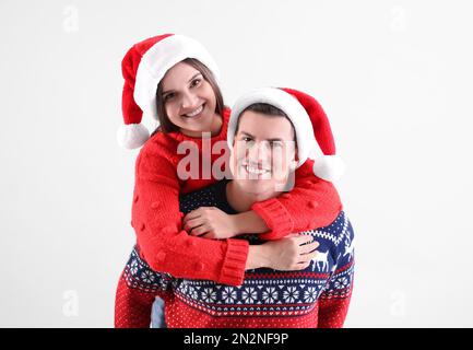 Wunderschönes glückliches Paar in Weihnachtsmannhüten und Weihnachtspullover auf hellem Hintergrund Stockfoto
