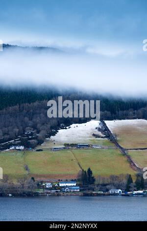 Loch Ness, Highlands, Schottland. Im Winter. Berge, seeufer und Felder teilweise mit Schnee bedeckt. Bauernhäuser, Felder, Weideland. Keine Menschen Stockfoto