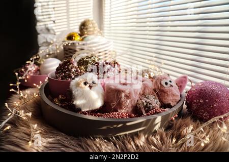 Wunderschöne Weihnachtsbaumkugeln, Spielzeug und Lichterketten auf der Fensterbank im Innenbereich Stockfoto