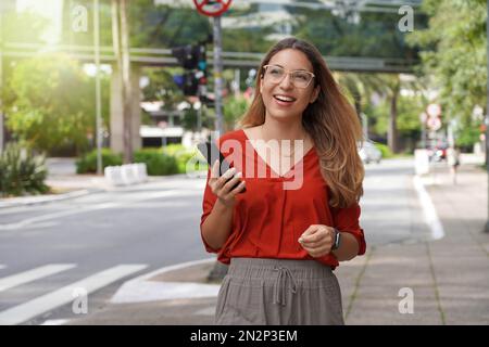 Lächelnde Geschäftsfrau mit Mobiltelefon, die in einer modernen, nachhaltigen Metropole unterwegs ist Stockfoto