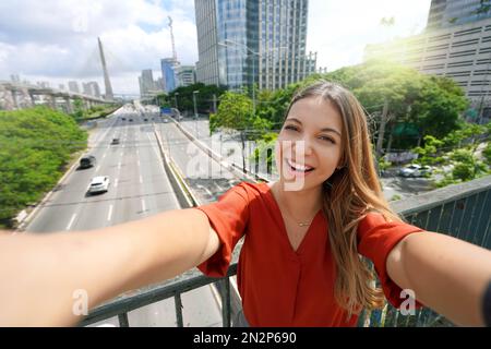 Tourismus in Sao Paulo. Ein wunderschönes lächelndes Mädchen macht Selbstporträts mit der Ponte Estaiada Bridge in der Metropole Sao Paulo, Brasilien. Stockfoto