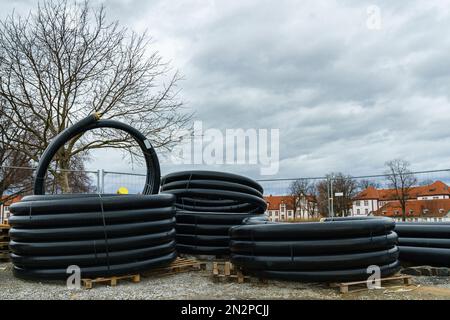 Rollen mit schwarzen Wellrohren liegen auf der Baustelle. Unter grauem, bewölktem Himmel. Stockfoto