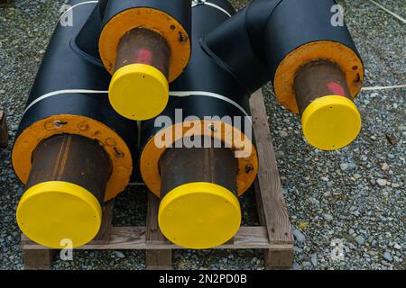 Schwarze isolierte Heizungsrohre mit gelben Kunststoffstopfen liegen auf einer Baustelle. Schließen. Stockfoto