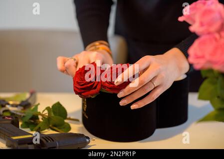 Nahaufnahme einer Frau, die am Valentinstag ein Blumenarrangement mit roten Rosen macht Stockfoto