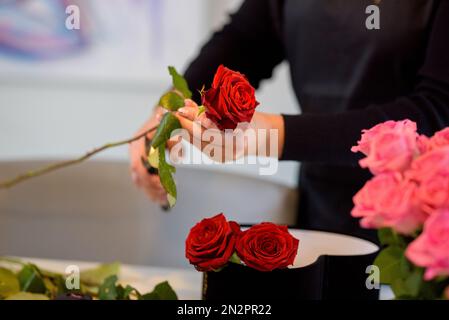 Nahaufnahme einer Frau, die am Valentinstag ein Blumenarrangement mit roten Rosen macht Stockfoto