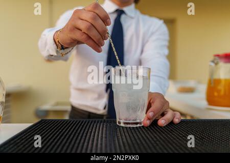 Ein Barkeeper bereitet einen köstlichen Cocktail mit einem Mischwerkzeug zu. Der Fokus liegt auf dem Glas und den geschickten Techniken des Barkeepers - Mittelteil Stockfoto