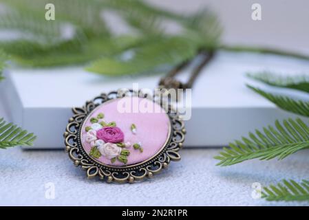 Nahaufnahme einer von Hand gestickten Halskette auf einer weißen Geschenkbox mit Tannenzweigen Stockfoto